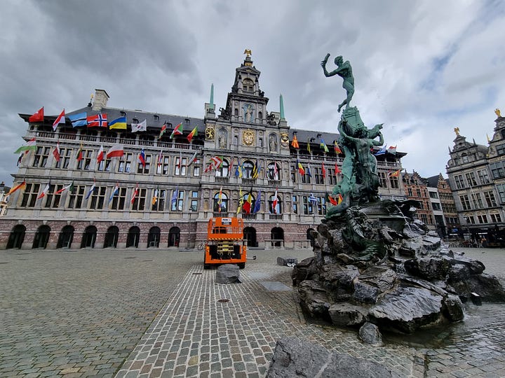 Photo 1: Fort Het Seen in the background with a statue of Lange Wrapper (a water spirit) towering over humans in the foreground. Photo 2: Antwerp Town Hall and statue of Brabo in the foreground throwing a severed hand. Photo 3: Photo from inside the Antwerp Bourse. Photo 4: Dave going down the wooden escalator in the St Anna tunnel. 