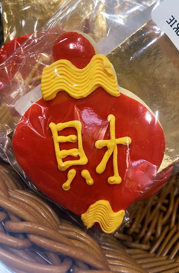 Left: cookie in shape of Chinese red lantern, with word for 'prosperity' written in Chinese. Right: Chinese red packet and gold coin to celebrate Lunar New Year.