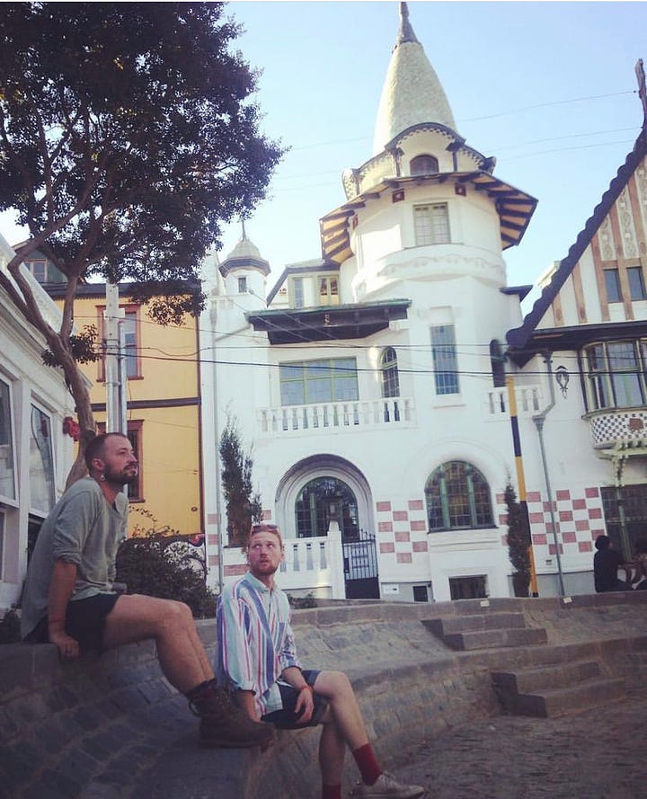 A victorian touret glows during sunset in Playa Ancha while two  stylish men chat in front of Baburizza Palace. 