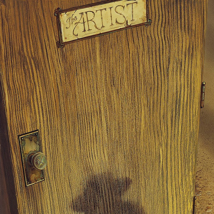 LEFT: Close detail of the yellow and brown woodgrain of a door. At the top is a sign with cracking paint that reads"The ARTIST." On the lower left a doorknob marked with the X of two crossing paint brushes sits on a metal plate rusted and peeling. RIGHT: Detail from THE ARTIST'S DOOR featuring Roland sitting cross legged with head in hands. His cowboy hat is hand stitched. His head dips, and the long ends of a dark handkerchief tied at his neck fall on the back of his light gray shirt. His gun is holstered at his hip and the brass heads of bullets wind around the back of his waist.