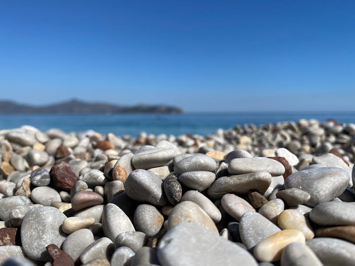 Island images - close up of pebbles with sea in the distance and yellow flowers.