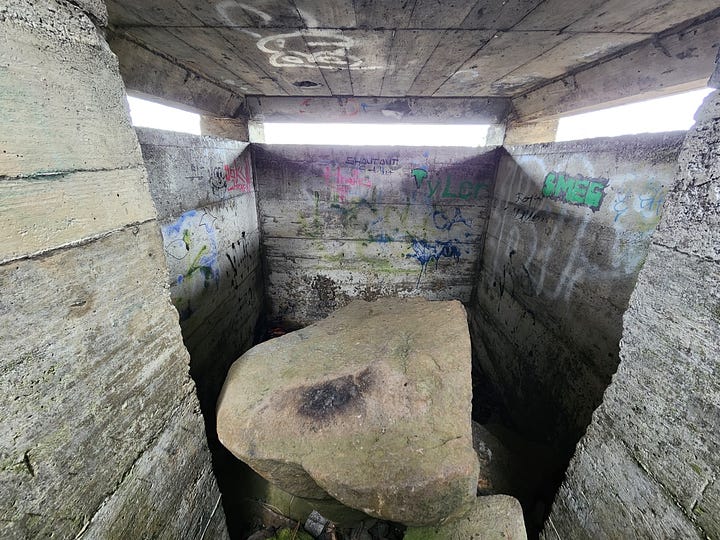 A concrete pillbox bunker on a grassy hillside with lichen-covered boulders and graffiti, and the inside of the pillbox, grey walls with blinding white sunlight through the slits, and boulders left by vandals.