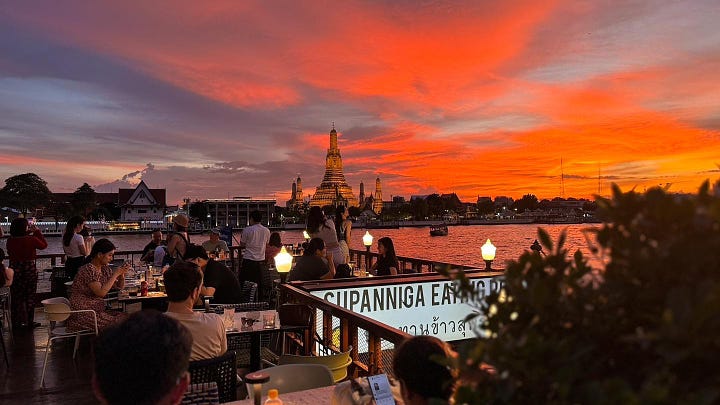 Glimmering gold turrets rise into the blue skies of Bankok and diners relax at sunset with a neon sky overlooking the  Chao Phraya River.view of 