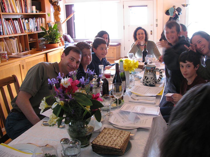 long table with flowers and wine bottles and haggadah booklets and lots of happy people