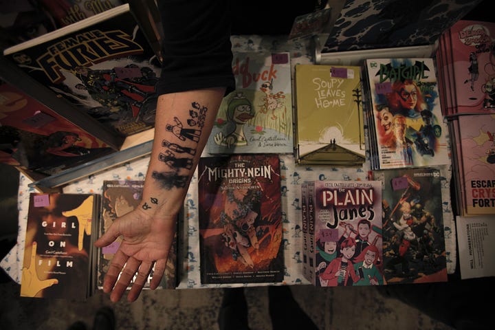 Cecil's arm sporting a tattoo of a little person on top of a stack of books. Next to an image of a flyer for the Oper'Actuel in text.