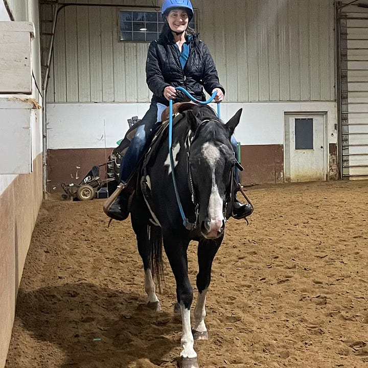 Woman in black coat and blue riding helmet with black horse with white nose