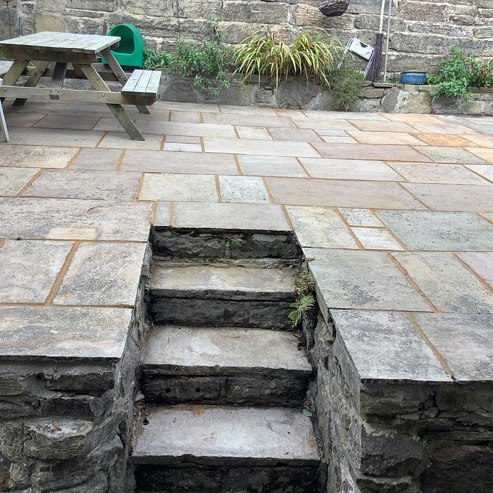 Five pictures of the patio in various stages of repair. First being pressure washed, second, three men is hi-vis clothing are gathered round one flag ‘discussing’ the work needed, third is a pic of lots of lifted flags and a lot of mess, fourth is he revealed steps of York stone and the relaid and regrouted old flags of many colours, the first is a picture of fags that have been regrouted, the grout is ina contrasting colour. 