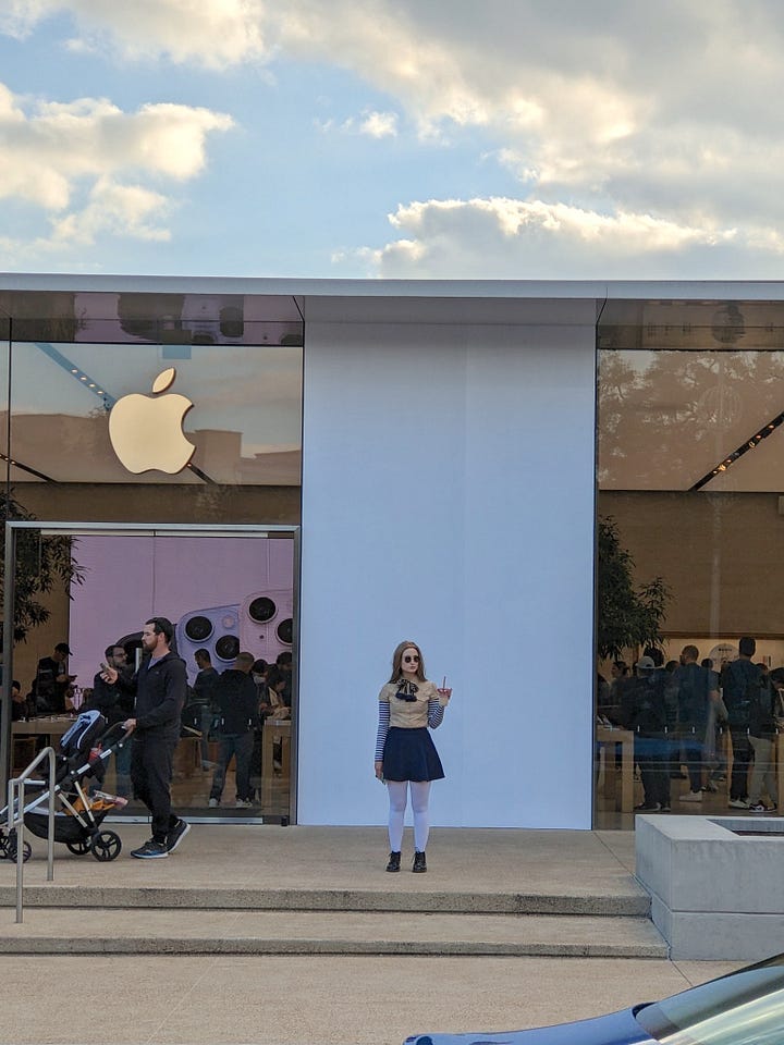 4 photos of me as M3gan at The Domain. M3gan drinking bubble tea, M3gan in front of a "LOVE" mural, M3gan in front of the Apple store, and M3gan looking into the Coach store.