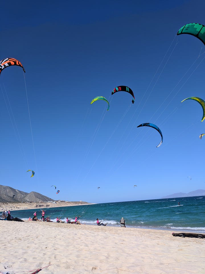 Left - beach with pink cocktail and kites in the air. Right - beach with mountain in the background and kites in the air about to start a competition.