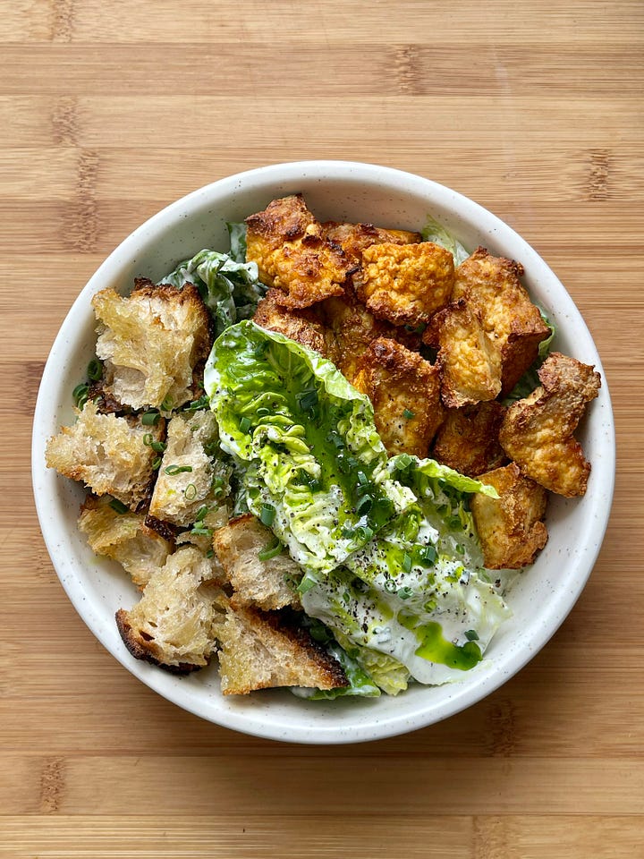 Two side-by-side images showing Buffalo tofu salad in a speckled bowl. The tofu in the salad on the left is coated in lots of Frank's Red Hot-based Buffalo sauce and drizzled with homemade ranch dressing. The salad on the right has non-glazed Buffalo tofu and includes croutons.