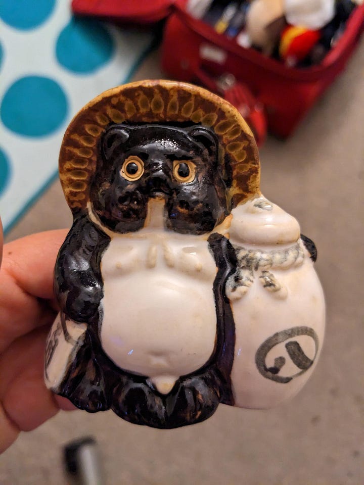 A side by side comparison of an actual tanuki statue with a drawing of the idol of misfortune.