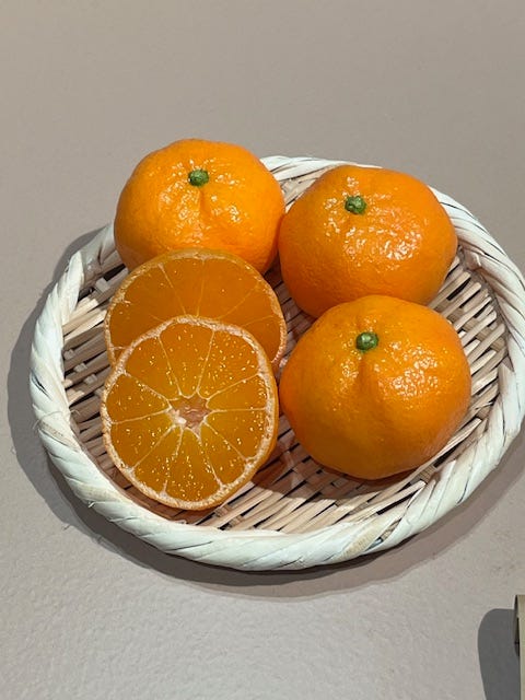 on the right is a plate with three replica mandarins and two halves, and on the left is an example of fake food described as orange slices on pizza