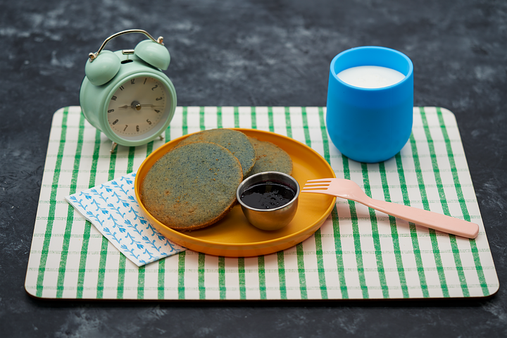 L: Brown tepary beans in wooden bowl; R: Tocabe Blue Corn pancakes on orange plate on green and white checkered placement