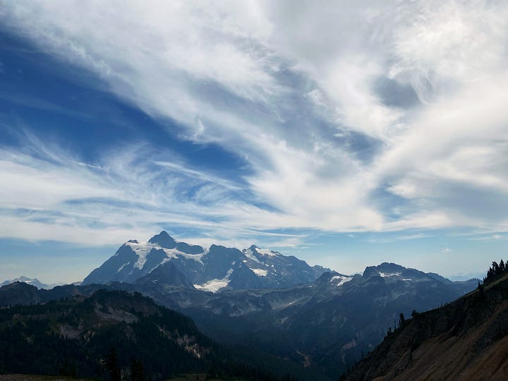 Two photographs of the mountains at Artist Point, WA. One taken on a film camera with a small girl in the 1970s and one taken on an iPhone of mountains only in the 2020s.