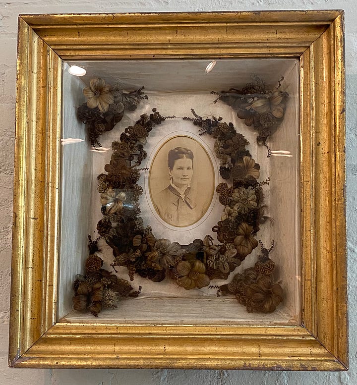 a shadow box with the deceased, surrounded by human hair fashioned like flora plus an interpretive sign