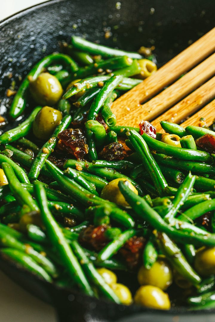 Green beans, olives, and dates in a pan; chicken nestled into the vegetables.