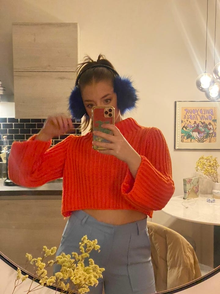 Left: Kelly in a checkered puffer coat layered on top of an orange crop top. Right: Kelly in a cropped orange sweater, baby blue pants, and royal blue earmuffs. A slay, your honor.