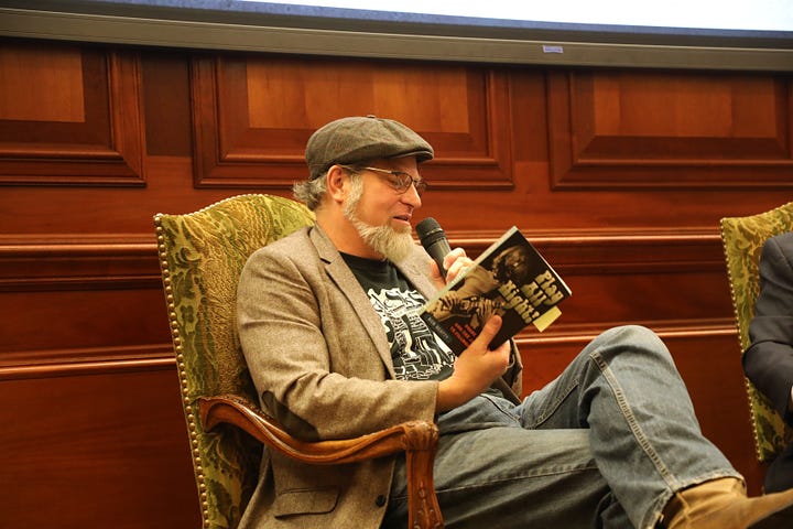 Bob Beatty (left) and Steve Murray (right) sit in chairs. Bob is wearing a hat, a tweed coat with elbow patches, a black Muscle Shoals Sound tshirt, blue jeans, and boots. Steve is in a gray suit with a white shirt. 