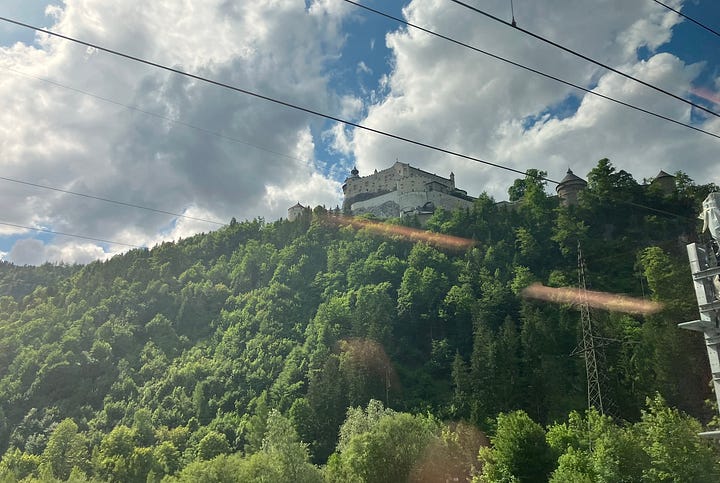 Beautiful views of mountains covered in trees, with a snowy cap in the background, and a castle perched on a hill