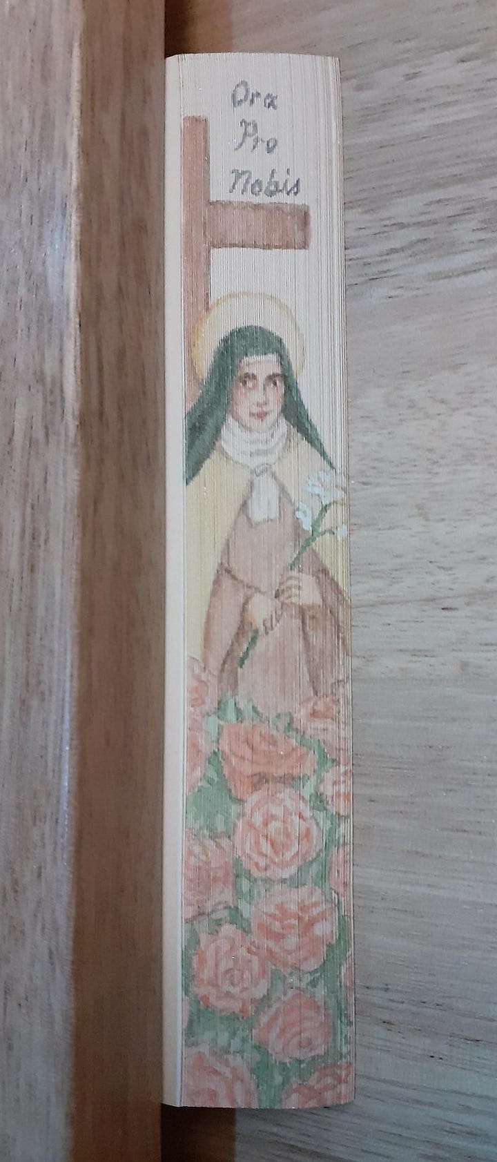 A painting of St. Therese of Lisieux on the fore-edge of a small gilded notebook