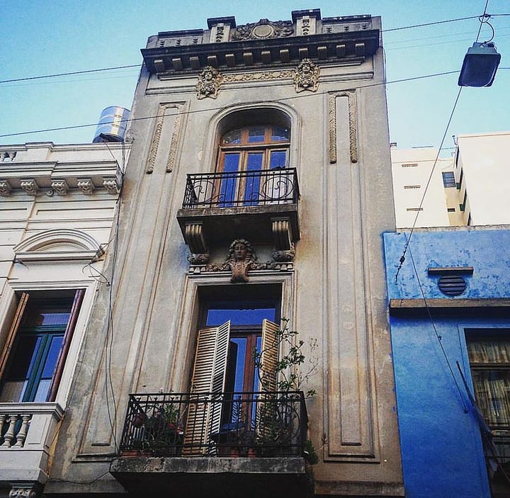 Two handsome gay men sip cocktails in front of Pride Cafe. An ornate  apartment in San Telmo has wrought iron balconies traipsed in flora, and French doors with Ventian blinds.