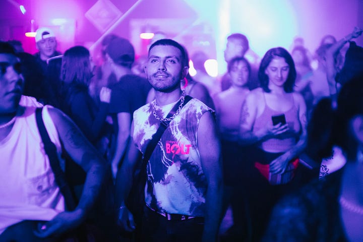 A handsome Chilean dances under the neon lights at Alto San Andres. The dancefloor  is glowing with pink light and sweaty ravers.