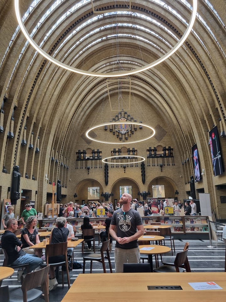 Photo 1: Canal in Utrecht showing people sitting outside enjoying bars and restaurants directly next to the canal. Photo 2: Dave looking up a the ceiling of the library which is domed and has circular light fixtures.