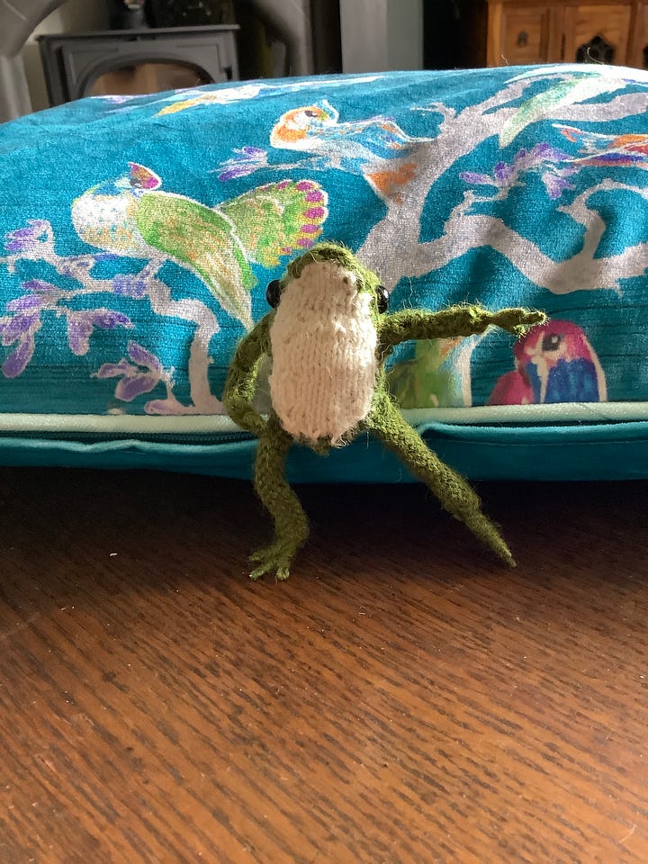 A tiny knitted frog in a cream jumper in a variety of poses, one without the jumpers and looking balletic