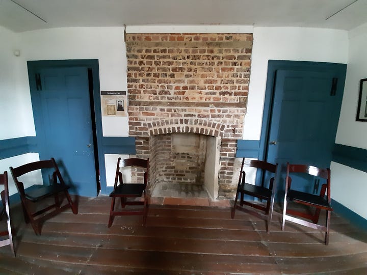 The interior of Hampton shows large rooms with wooden floors. The paint is blue. The fireplace is brick, with chairs sitting around.