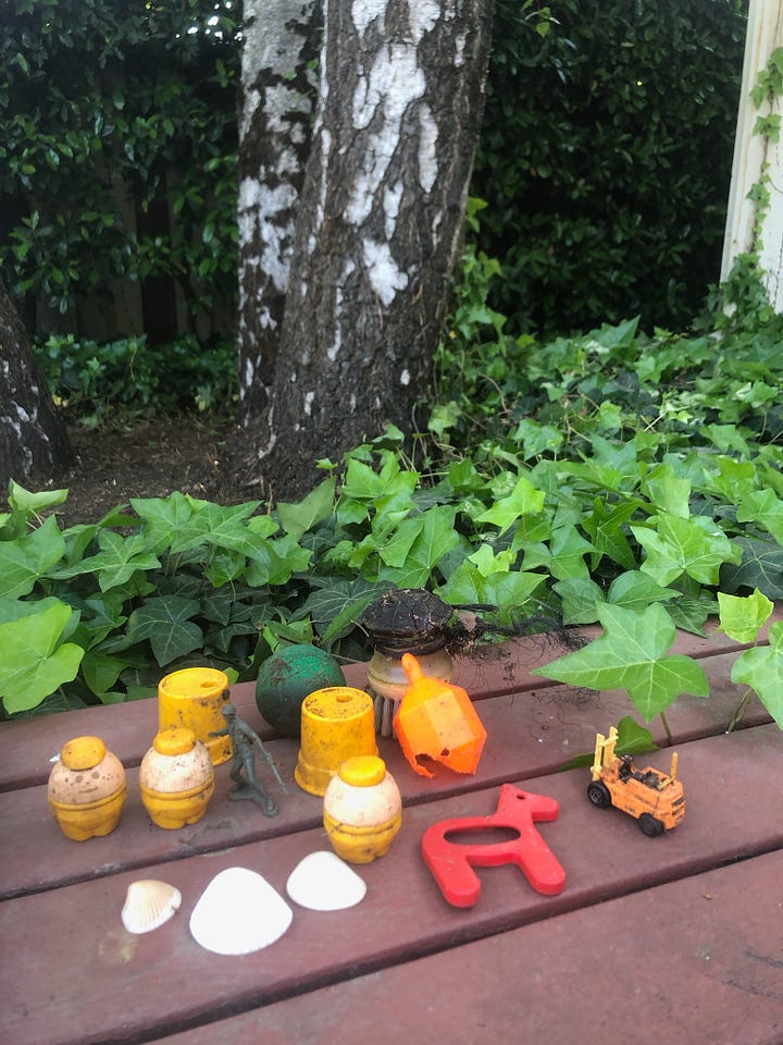Image one shows three birch trees surrounded by Ivy and gardening tools, the second image shows an up close looks at small vintage children's toys found inside of the Ivy during removal