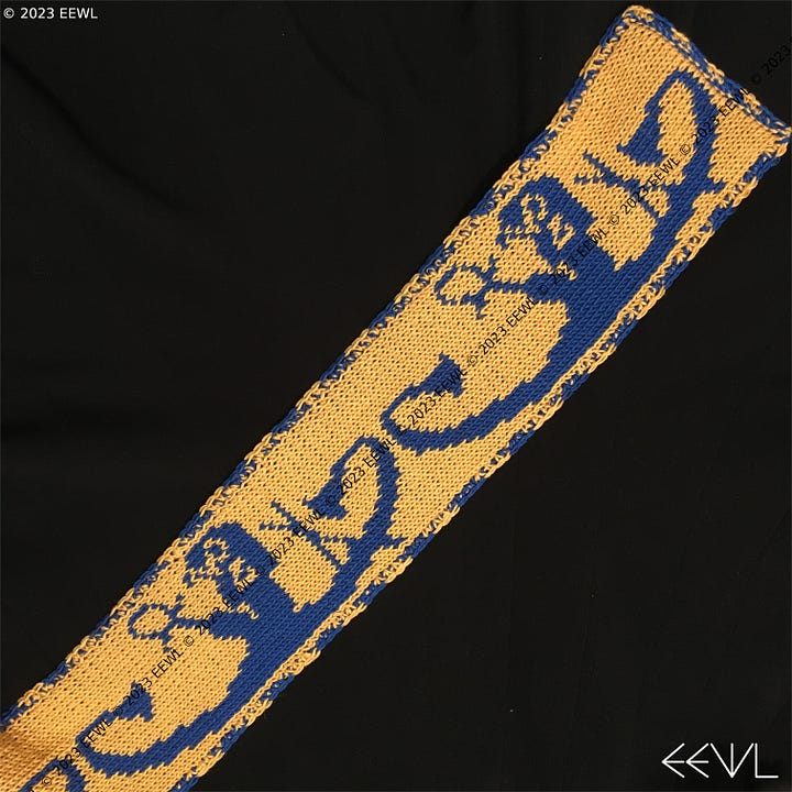 Images of both sides of a blue and yellow hand-knitted scarf. The pattern on the scarf features the Ancient Egyptian sun god Ra traveling across the sky in his solar barque, or boat.