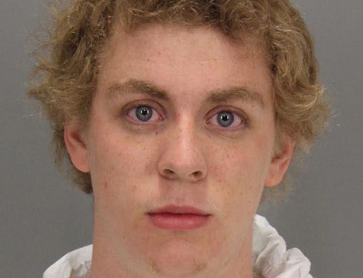 Booking photo of a young man with curly blond hair against a gray wall