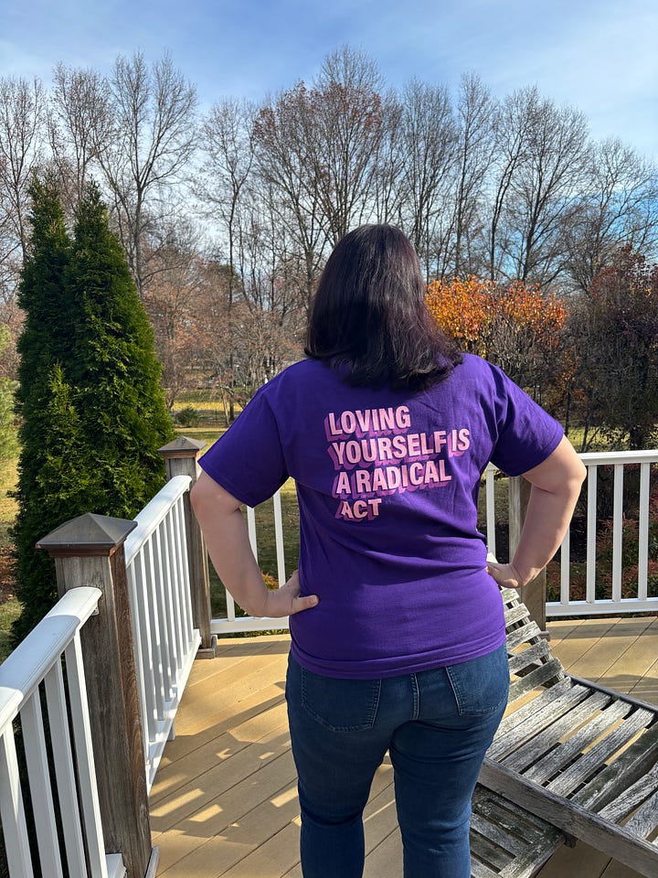 Claire wears a royal purple t-shirt with the Empire Waist logo. Back of t-shirt reads "Loving Yourself is a Radical Act."