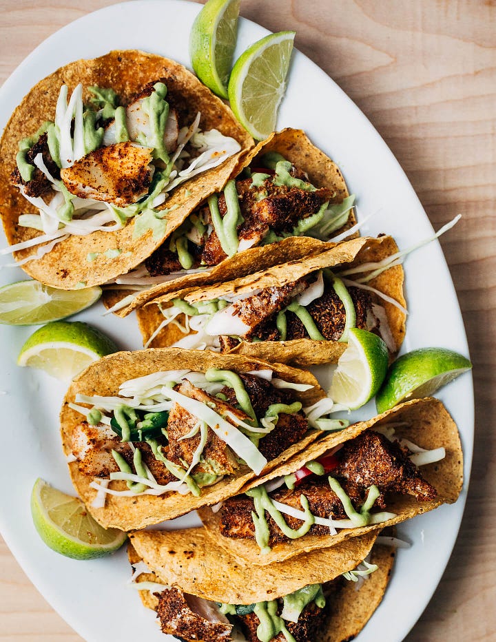 A platter with briased cabbed wedges on the left, and a platter of tacos with golden baked fish, cabbage, and avocado sauce on the right.