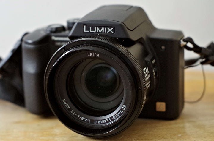 The 1:3.5-5.5 on the first camera shows the F-number is 3.5 at the widest and 5.5 at full zoom. The 2.8 on the Lumix, shows the widest F-number is 2.8 throughout the range of the zoom.