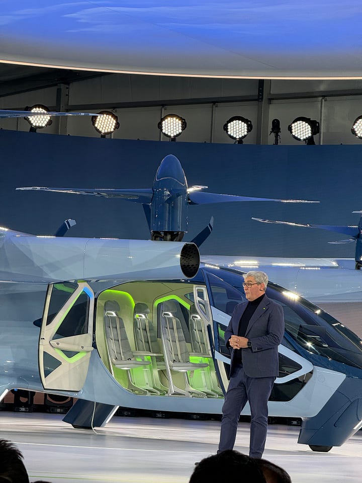 The Supernal S-A2, a sleek aircraft on a round stage surrounded by lights. One photo shows a green-lit interior with four passenger seats.