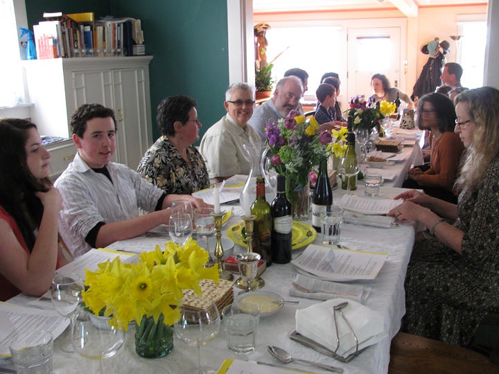 long table with flowers and wine bottles and haggadah booklets and lots of happy people