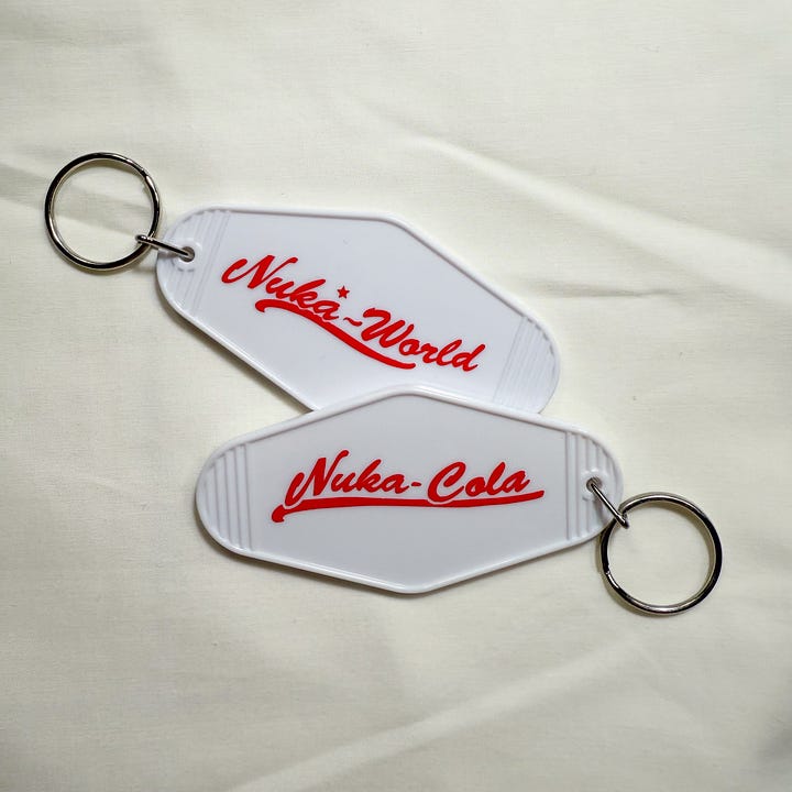 White hotel-style keychains with red text saying Nuka World and Nuka Cola