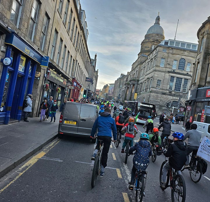 A grid of four photographs depicting a mass of between fifty and one hundred cyclists, mostly in helmets and jackets, making their way as a unit through the streets of Edinburgh on a clear, cold day 