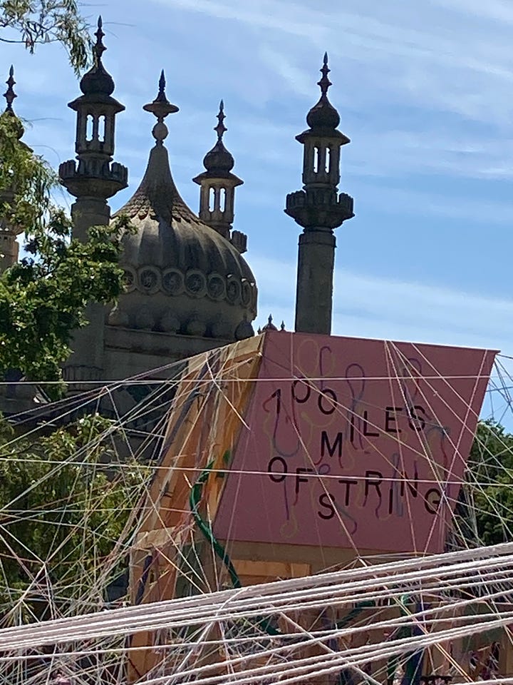 100 Miles of String sign on a large wooden board with tangled string around it in the foreground /Brighton Pavilion in the background; A thick tangle of string and a child in the foreground