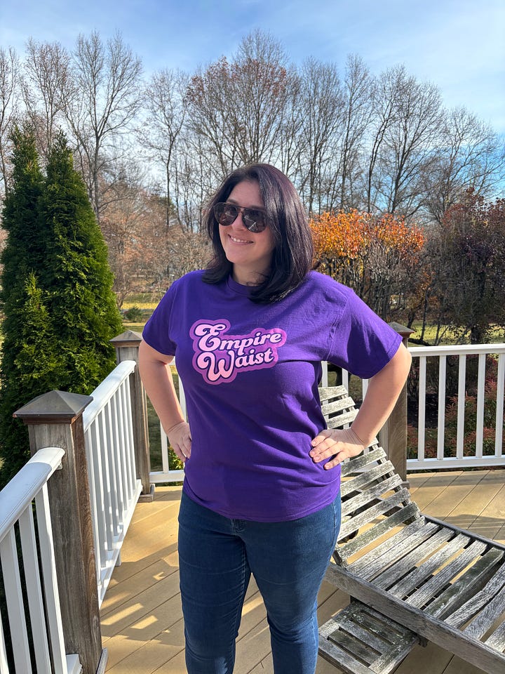 Claire wears a royal purple t-shirt with the Empire Waist logo. Back of t-shirt reads "Loving Yourself is a Radical Act."