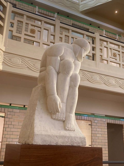 Wide shot of swimming pool gallery; Hommes Dames pool entrance; white marble sculpture of bather; plaster of Paris sculpture of torso with red mushroom cloud in place of the head