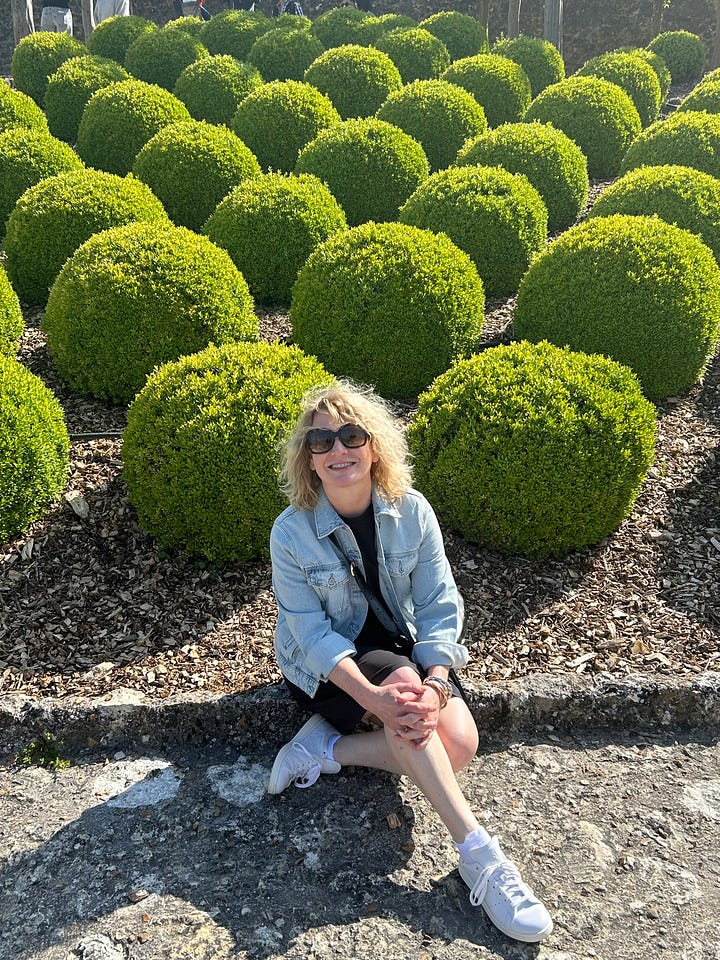 Karen Bussen seated in a garden with topiaries and grapevines