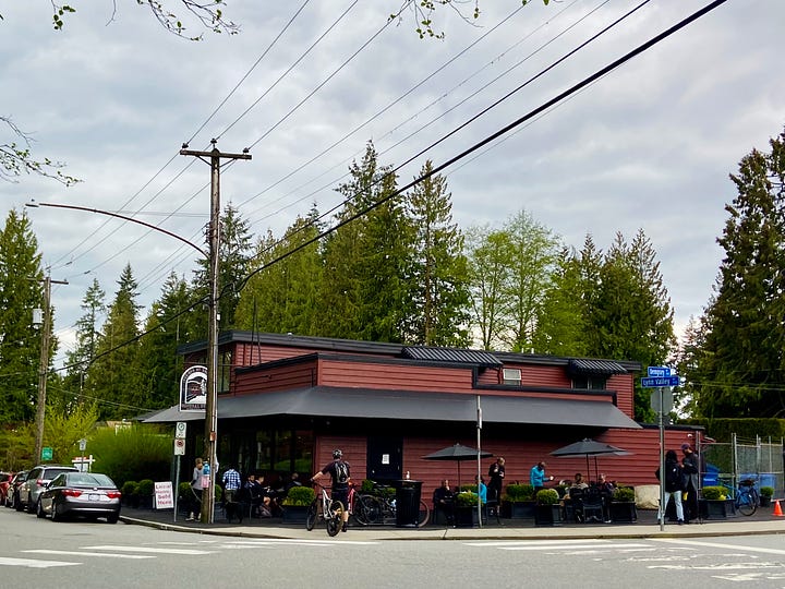 left: small, red, one-story general store; right: residential street lined with fir trees.