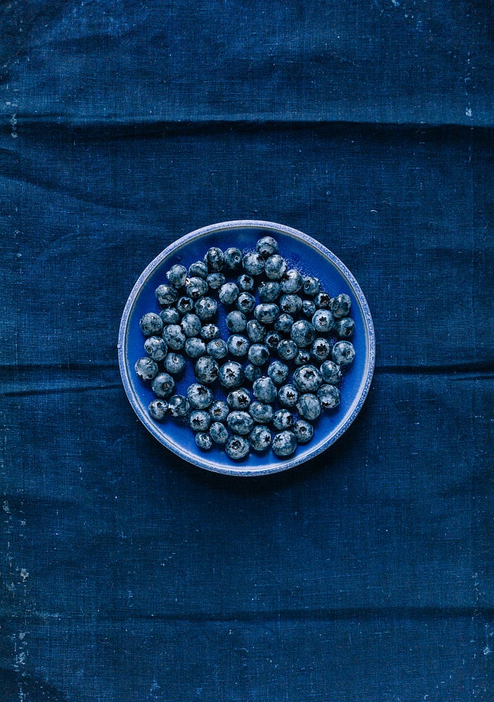 Indigo blue fabric with a bowl of blueberries. A section of raw honeycomb