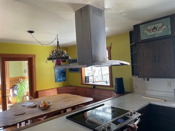 Two photos of before and after a kitchen remodel. Dark cabints on the left and photo on right shows the removed with a new free hanging stove fan.