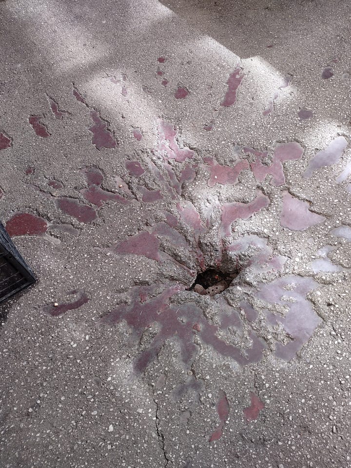 Pictures of a red splotch mark on the ground. It is the indent of a bomb indentation.