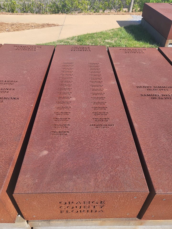 Bronze of Rosa Parks, historic marker by MLK's Dexter Avenue Baptist Church, names of justice nonprofits etched into a black wall, tomb-like structures listing those killed by lynching, shown laying like a coffin and hanging above