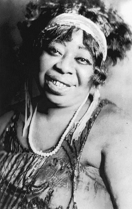 Two Black women blues singers from the 1920s, smiling and dressed in fancy evening wear