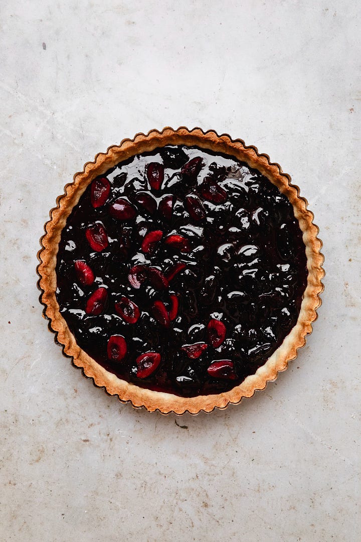 Vegan fresh cherry frangipane tart, including a pastry shell, cherry jam, cherries, almond frangipane and flaked almonds 